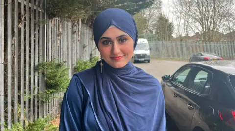 Sarosh is wearing a blue headscarf and matching top/robe with gold earrings and make-up