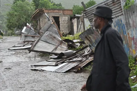 EPA A man walks in front of a house damaged by Hurricane Melissa in Kingston, Jamaica, on 28 October 2025