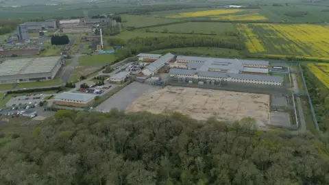 Ant Saddington/BBC An aerial view of Yarl's Wood large secure facility surrounded by farmland and woodland, with fenced buildings, access roads and yellow rapeseed fields visible nearby.