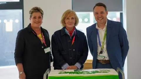 North Somerset Council Three people smiling at the camera standing behind the cake on a trolley