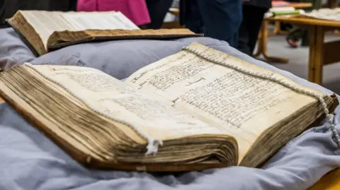 West Northamptonshire Council An old book resting on a cushion. The book is open. Another book is behind it, again open.