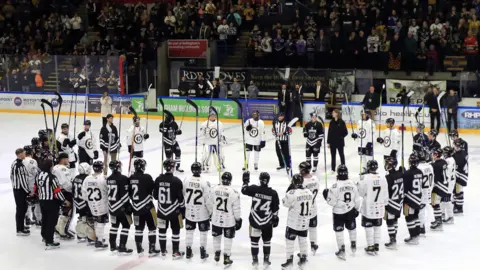 PA Media A ring of ice hockey players in white and black holding their sticks in the air