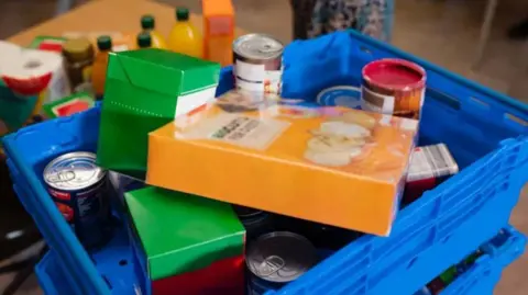 A basket of supermarket items, including cereal and tins of soup.