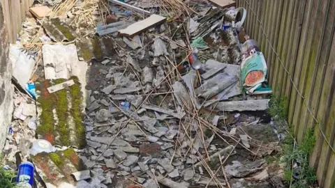 William Banks An image of a back alley with piles of broken asbestos concrete and other rubbish.