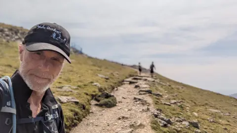 Andrew Lamb Andrew Lamb in selfie walking up mountain in sunny conditions