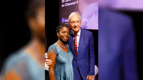 Dr Precious Lunga (left), wearing a blue dress and Jon Snow (right) wearing a blue suit.