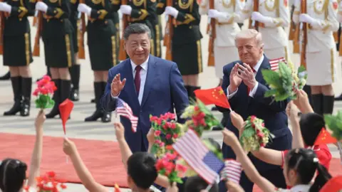 Xi and Trump wave while walking down a red carpet in front of schoolchildren waving flags and a row of military officers standing to attention at the Great Hall of the People in Beijing on Thursday.