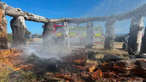 DWFRS The burnt remains of the 'Woodhenge' structure with a fire engine in the background.