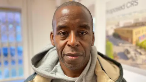 Trevor is wearing a grey hoodie and a jacket