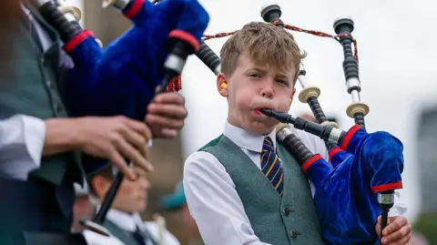 Getty Images A young male piper playing the bagpipes. His cheeks are puffed out as he plays. He is wearing a traditional piper outfit 