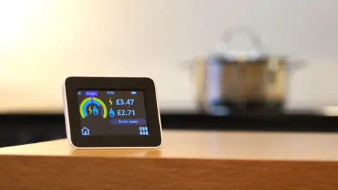 Electricity smart meter on a kitchen counter with a pot on a stove in the background.