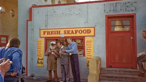 Only Fools and Horses Appreciation Society Three characters stand outside a “Fresh Seafood” shop - Uncle Albert, Del Boy and Rodney Trotter - with menu boards and a closed door visible.