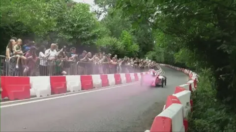 Burghfield Box-kart Bash A pink kart riding down a hill with people watching from the side behind railings