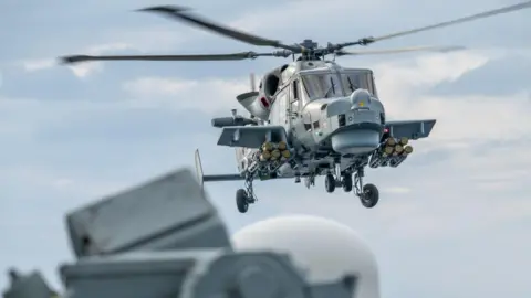 MoD Navy grey/blue helicopter carrying missiles whilst in flight 