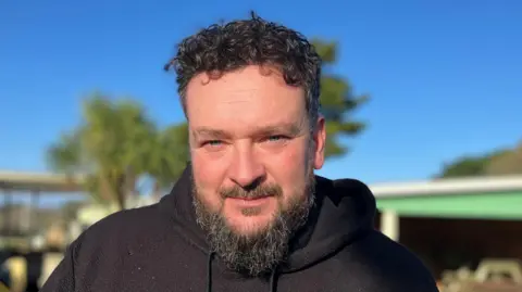 Man smiling at the camera with curly hair and a beard