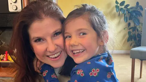 Katy and Molly, both with dark brown straight hair, embrace and smile.