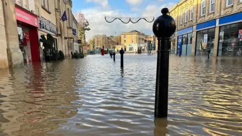 Chippenham town centre after flooding from Storm Bert. Bollards along the street can be seen, as well as businesses along either side of the road. They are all closed due to the flood. 