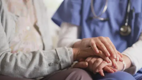 We can see a care resident's hand being held by a care worker.