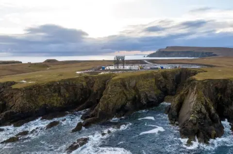 RFA UK SaxaVord Spaceport is positioned near the coastline. Waves lap the cliffs and the land above is flat, with a launching pad for the spaceport.