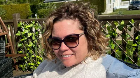A close-up image of a woman wearing sunglasses. She is smiling and looking into the camera.