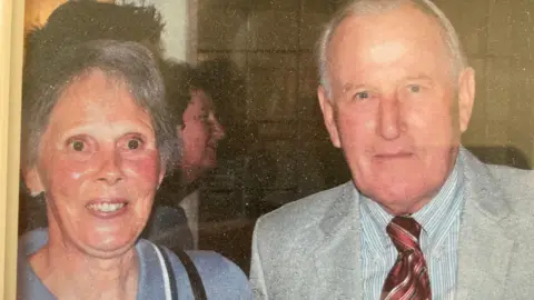 An old photo of Peter and Diana together. Both look at the camera, dressed smartly.