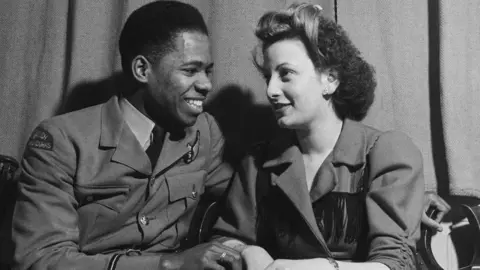 Getty Images A young couple, a black man in an army uniform and a white woman in a smart coat, in Edinburgh Hall at an evening event held during the Fifth Pan-African Congress, held at Chorlton-upon-Medlock Town Hall in Manchester