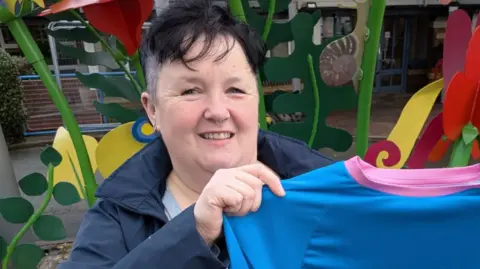 A woman with short dark hair and a blue top holding a blue tshirt