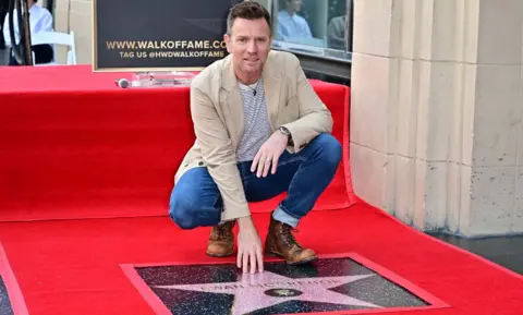 Getty Images British histrion  Ewan McGregor touches his prima  during his Hollywood Walk of Fame Star ceremonial  successful  Hollywood, California. He is wearing brownish  boots, jeans and a beige jacket.