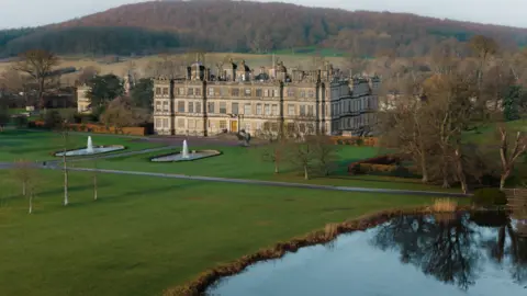 Tom Anders/Longleat A drone shot of Longleat house in the middle distance with a lake in the foreground and a wooded hill in the background