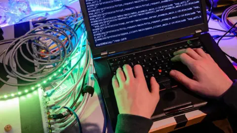 Getty Images A stock image showing a man typing complicated coding on a black laptop. Beside it is a silver hard drive with lots of wires coming out of it.
