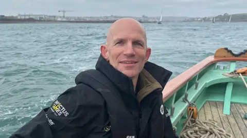 Mike Trebilcock sat on boat and looking straight at the camera and smiling. 