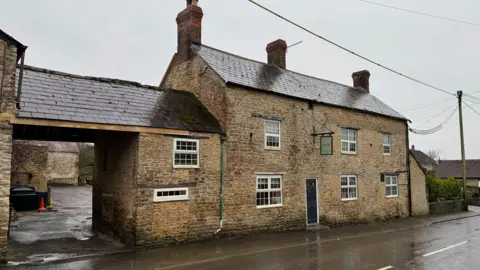Bricked building on the side of the road. It's an older building with a green sign hanging down from the edge of the building.
