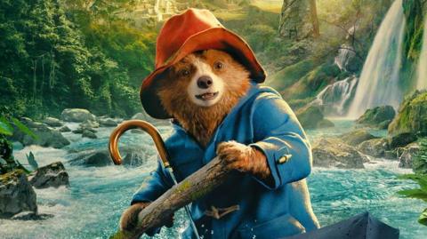 Paddington in Peru poster. Paddington bear is on a boat, on a river, which is running through a rainforest. 