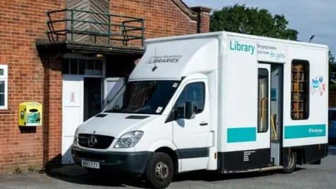 A white van with 'West Berkshire libraries' written on the front, parked outside a brick building.