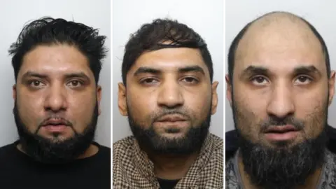 A composite of three mugshots placed side by side. Amar Ilyas on the left is shown from the shoulders upward, facing directly toward the camera. He has dark hair styled upward and slightly back, along with a full beard and moustache. He is wearing a dark top, and the face is evenly lit, with no strong shadows. In the centre portrait, Kamran Ilyas is presented in a similar head-and-shoulders format, also facing forward. He has short, dark hair and a full beard and moustache. The clothing appears to be a brown or patterned garment or shirt.
In the right portrait, Kamar Ilyas is shown with very little or no hair on the head and a full beard. He is wearing a dark or muted jacket or top.
