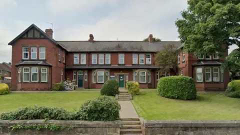 Primrose Lodge. The building is a large red brick detached property. It has a large green lawn and has two floors.