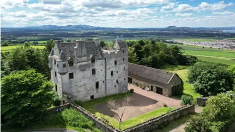 Savills A Scottish Castle over a number of stories standing in the countryside with a village and hills in the distance