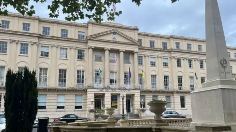 The exterior of Municipal Offices in Cheltenham, a large regency building with flags outside.