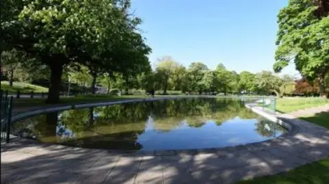 The long, circular pool is surrounded by grass and some trees