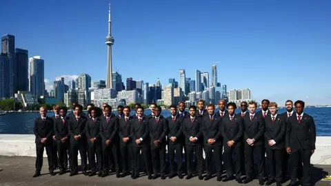 Getty Images Team Canada pose along the waterfront after arriving at Billy Bishop Toronto City Airport. The CN Toer and skyscrapers in downtown Toronto are behind them.