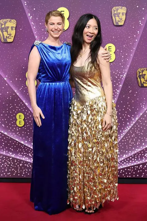 Getty Images Jessie Buckley in a long blue dress and Chloé Zhao in a gold dress