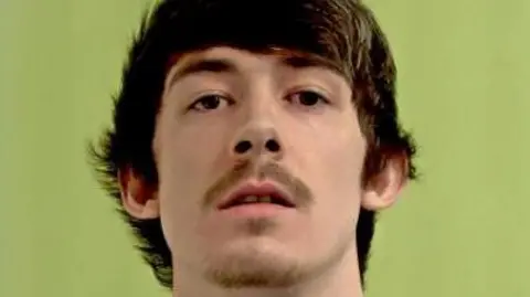 IOM CONSTABULARY Police mugshot of Louis Thomas, who has short brown hair with a fringe and a thin moustache and beard on his chin.