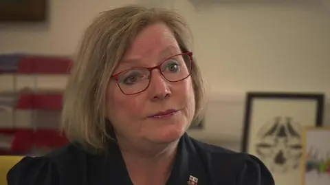 A woman in a black shirt with red glasses looking at the camera