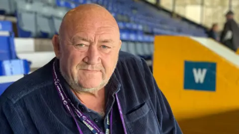 John 'Willo' Williams sitting in the stands of an empty football stadium.