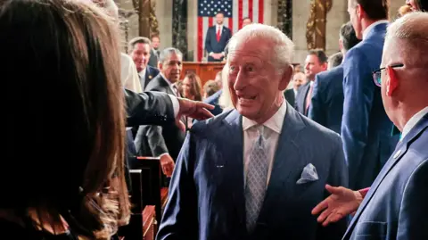 King Charles, with a grin on his face, walks by lawmakers in US Congress after delivering his speech, with US Vice-President JD Vance and a US flag visible distantly behind him