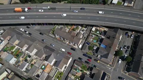 An overhead image from a drone showing how close to the M4 motorway the houses and gardens are. The image shows the motorway at the top of the image passing over the garden of a row of terraced houses