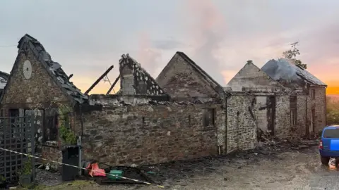 Launceston Community Fire Station A house severely damaged by fire. There is smoke coming from the remnants of the roof of the building, which is largely open at the top due to fire damage.