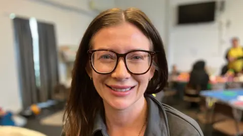 A woman with brown hair and glasses smiling and looking into the camera