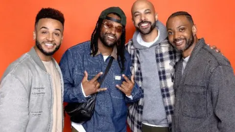Four members of JLS smiling against an orange background