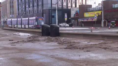 Debris covers a large section of the promenade, with a tram and Coral Island seen in the background.